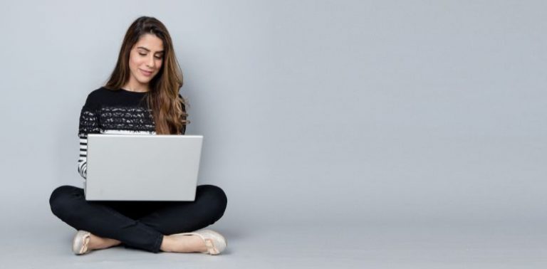 A woman sitting on the floor, using a laptop.