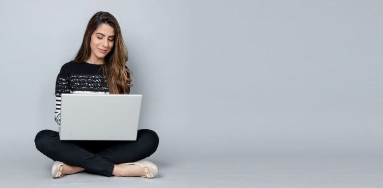 A woman sitting on the floor, using a laptop.