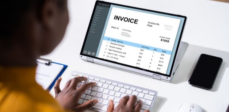 A woman typing, looking at a tablet screen that is displaying an invoice.