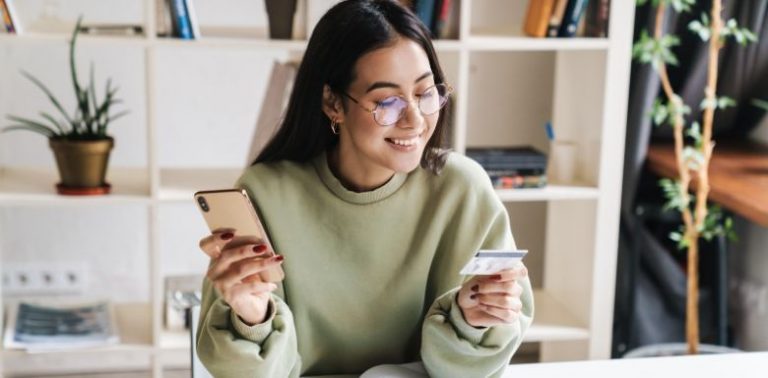 A woman holding a phone in one hand, and her credit card in the other hand.