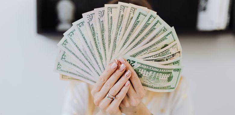 A woman holding a handful of cash bills in front of her face.
