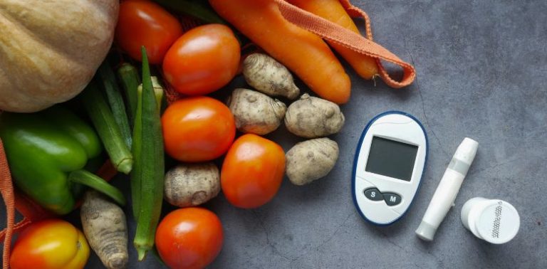 Fresh vegetables on a table with an insulin monitor and other diabetic supplies.