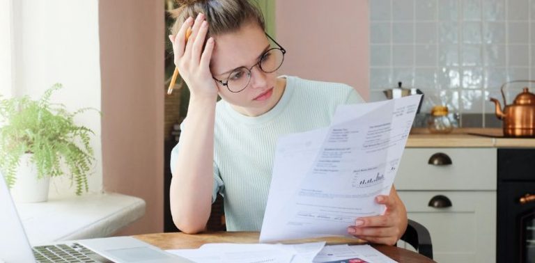A woman sitting at a table covered in paperwork, looking at a financial statement.