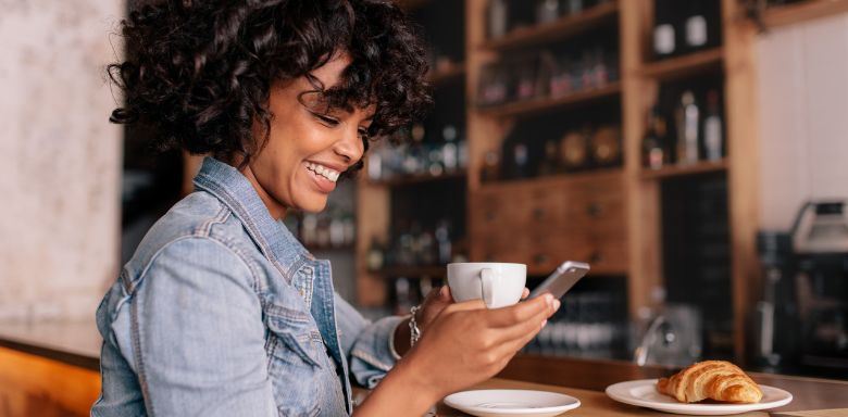 A woman sitting at a cafe table, holding a cell phone.