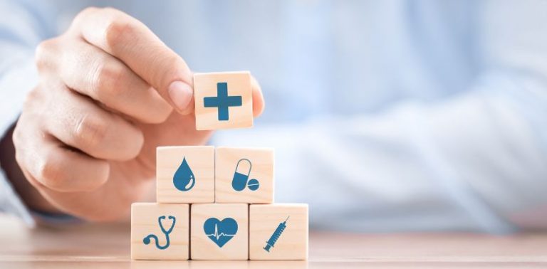 A hand holding small wooden blocks with blue health and medical symbols on them.